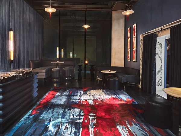 Inside of the glass pavilion of the Blue Bar with a red and blue abstract rug, a DJ decks and low blue bar stools